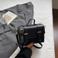 Schwarze quadratische Umhängetasche aus Leder mit goldenen Schnallen auf weißem Untergrund - Schwarz