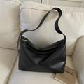 Detalle de bolso hobo negro minimalista con cremallera y hebilla dorada sobre el sofá - Negro