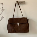 Primer plano de bolso tote vintage marrón oscuro con hebilla plateada en percha de metal - Marrón