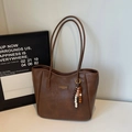 Detail der dunkelbraunen Totetasche aus Kunstleder mit Perlenquaste und Logo-Plakette - Braun
