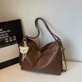 Detail of a brown leather tote bag with gold hardware and a cute white plush bear pendant - Brown