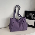 Detail view of purple nylon tote bag featuring side pockets and round metal logo emblem - Purple