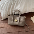Detail of taupe pebbled leather handbag with gold circular twist-lock closure on wooden floor - Elephant Gray
