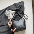 Borsa a secchiello in pelle nera alla moda con manico e ciondolo a peluche su sfondo di abito - Nero