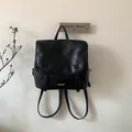 Dettaglio di zaino vintage in ecopelle nera con logo metallico e finitura ruvida - Nero