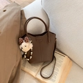 Detail der dunkelbraunen Eimer-Tasche aus Leder mit Bärenanhänger auf Buch - Kaffeebraun (Mit Anhänger)