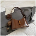Detail view of brown leather tote bag with golden twist lock and plush charm on suit background - Brown with Pendant