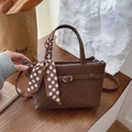 Brown woven texture handbag with polka dot scarf and adjustable strap on wood table - Brown