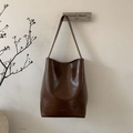 Detail der dunkelbraunen Vintage-Beuteltasche aus glänzendem Kunstleder an einer weißen Wand - Braun