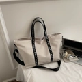 Dettaglio della borsa tote beige con cinturini con borchie nere e tracolla larga - Bianco Sporco