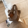 Détail du sac seau en cuir marron avec breloque en cœur et pompon sur un canapé - Avec Pendentif / Marron