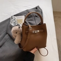 Close-up of brown lychee grain leather bucket bag with silver lock and plush bunny charm - With Charm / Brown