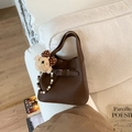 Détail du sac seau en cuir café avec breloque ours en peluche et poignée perlée sur canapé - Café Avec Pendentif
