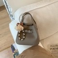 Détail du sac seau en cuir taupe avec charme d'ours posé sur un canapé en tweed - Gris Avec Pendentif