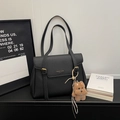 Detail of black pebbled leather tote bag featuring golden logo and cute plush puppy charm - With Charm / Black