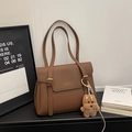 Detail of dark brown pebble leather tote bag with metallic buckles and plush puppy charm - With Charm / Brown