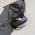 Schwarze Satteltasche aus Leder mit Metallschnalle und Herzanhänger auf grauem Stoff - Mit Anhänger / Schwarz