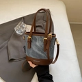 Blue denim bucket bag with brown leather trim and golden hardware held by hand - No Pendant / Blue