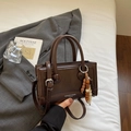 Détail d'un sac à main vintage marron foncé avec pendentif perlé sur literie blanche - Café avec Pendentif