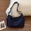 Detail of navy nylon messenger bag with multiple zippers and drawstrings on wood floor - Dark Blue