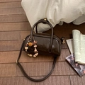 Detail einer glänzenden dunkelbraunen Zylindertasche mit Perlenanhänger auf Holz - Kaffee mit Anhänger