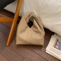 Dettaglio borsa beige in pelle martellata con manico a nodo su pavimento di legno - Cachi Scuro