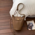 Détail du sac seau en cuir grainé marron avec finitions dorées sur parquet en bois - Marron