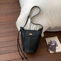Detalle de bolso bucket en cuero granulado negro con hebilla dorada sobre madera - Negro