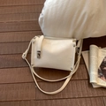 Close-up of cream square bag showing pleated texture and silver stud details on a wood floor - White