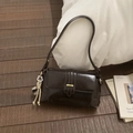 Close-up of dark brown glossy shoulder bag featuring golden buckles and a floral pendant - Coffee with Pendant