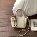 Detail of cream leather handbag with decorative plush puppy charm and textured surface - White with Pendant