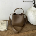 Braune Beuteltasche aus Leder mit breitem Griff auf Holztisch neben Keramikvase - Braun