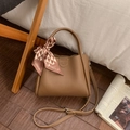 Detailed macro view of litchi texture brown bucket bag with a silk scarf tied on the handle - Brown