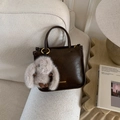 Detail of dark brown leather tote bag with plush bunny charm on a cream sofa - Coffee with Pendant