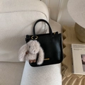 Close-up of black leather handbag with lychee texture and cute plush rabbit charm - Black with Pendant