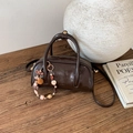 Close-up of vintage brown leather cylinder handbag with pearl charm on wooden surface - With Charm / Brown