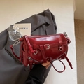 Dettaglio borsa cilindrica in pelle verniciata rossa con borchie e nappe metalliche - Borgogna
