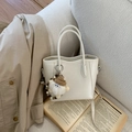 Dettaglio della mini borsa a secchiello beige con ciondolo a forma di mostro su divano - Bianco con ciondolo