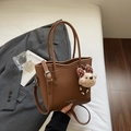 Brown lychee leather bucket bag with a plush bear charm and adjustable shoulder strap - With Charm / Brown
