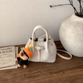 Dettaglio di una borsa a secchiello intrecciata crema con manici in pelle e ciondolo a cucciolo - Bianco con ciondolo