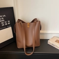 Détail du sac seau en cuir marron à motif litchi avec fermoir doré et fines bandoulières - café