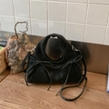 Detail shot of black suede cloud bag featuring decorative bows and round handle on wood - Black