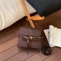 Detail of dark brown trapezoid handbag with decorative straps and gold buckles on wood floor - Brown