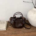 Close-up of glossy dark brown leather bucket bag with metallic drawstring and Paris logo - Coffee