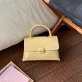 Dettaglio di una borsa in pelle giallo crema con trama liscia su pavimento in legno - Giallo