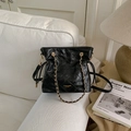 Detail of black quilted leather bucket bag with gold chain strap on a white sofa - Black without Pendant