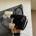 Bolso saco negro minimalista con textura plisada y un colgante de osito marrón - Negro