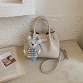 Dettaglio della borsa a secchiello beige con fibbie dorate e ciondolo a forma di orsetto - Bianco con ciondolo