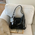 Detail of black faux leather tote with silver flower charm and grey silk decor on sofa - Black with Pendant