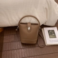Detail view of brown pebbled leather bucket bag with silver twist lock on dark wood floor - No Pendant / Brown